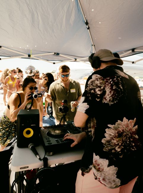 DJ spinning music at lively outdoor beach party under canopy.