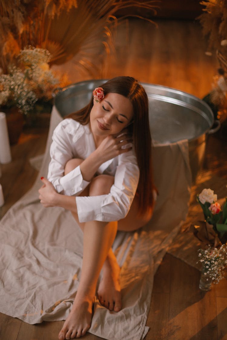 Woman Sitting On Floor Near Flowers At Home