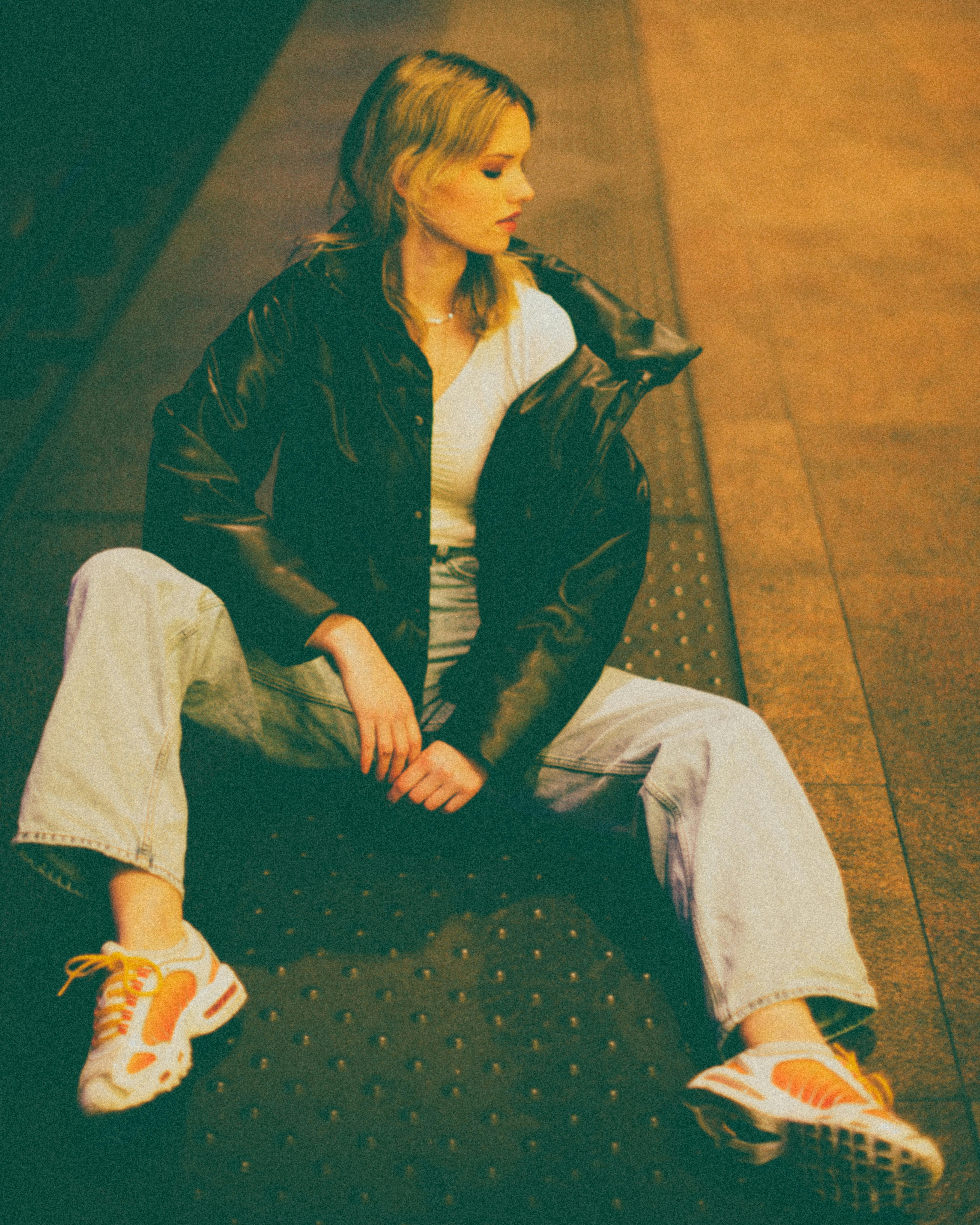 Young woman in casual fashion sitting on a subway platform. Urban lifestyle captured at night.