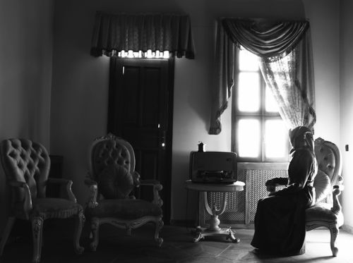 Free A woman sits in a vintage room with armchairs and a classic radio, creating a nostalgic mood. Stock Photo