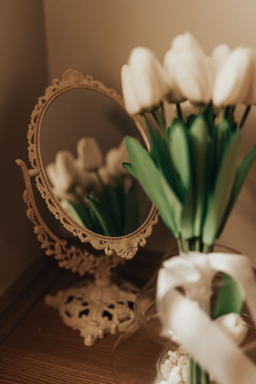 Free Delicate white tulips in a vase reflecting in an ornate vintage mirror, creating a warm and elegant composition. Stock Photo