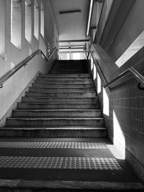 Free Monochrome photo of an indoor staircase with handrails leading upwards, capturing light and shadows. Stock Photo