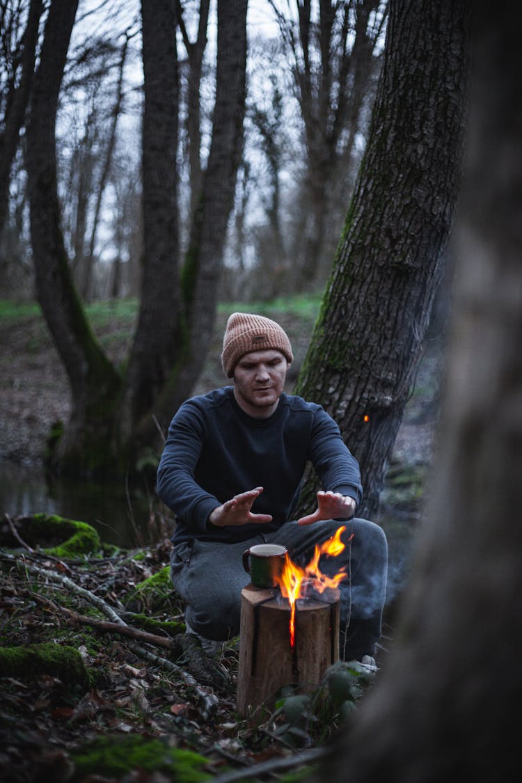 Man Warming Hands Near Fire In Forest