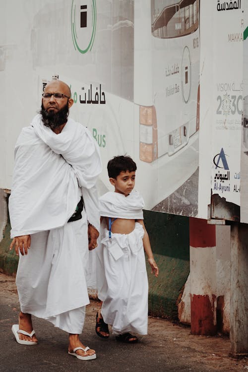 Father and Son in White Traditional Gowns Walking in Alley