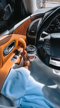 Close-up of a person holding coffee in a luxury car interior, showcasing elegance and style.