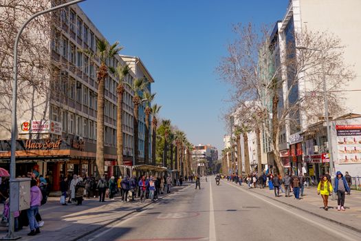 Busy city street in Izmir, Turkey, with pedestrians and palm trees under a bright sky.