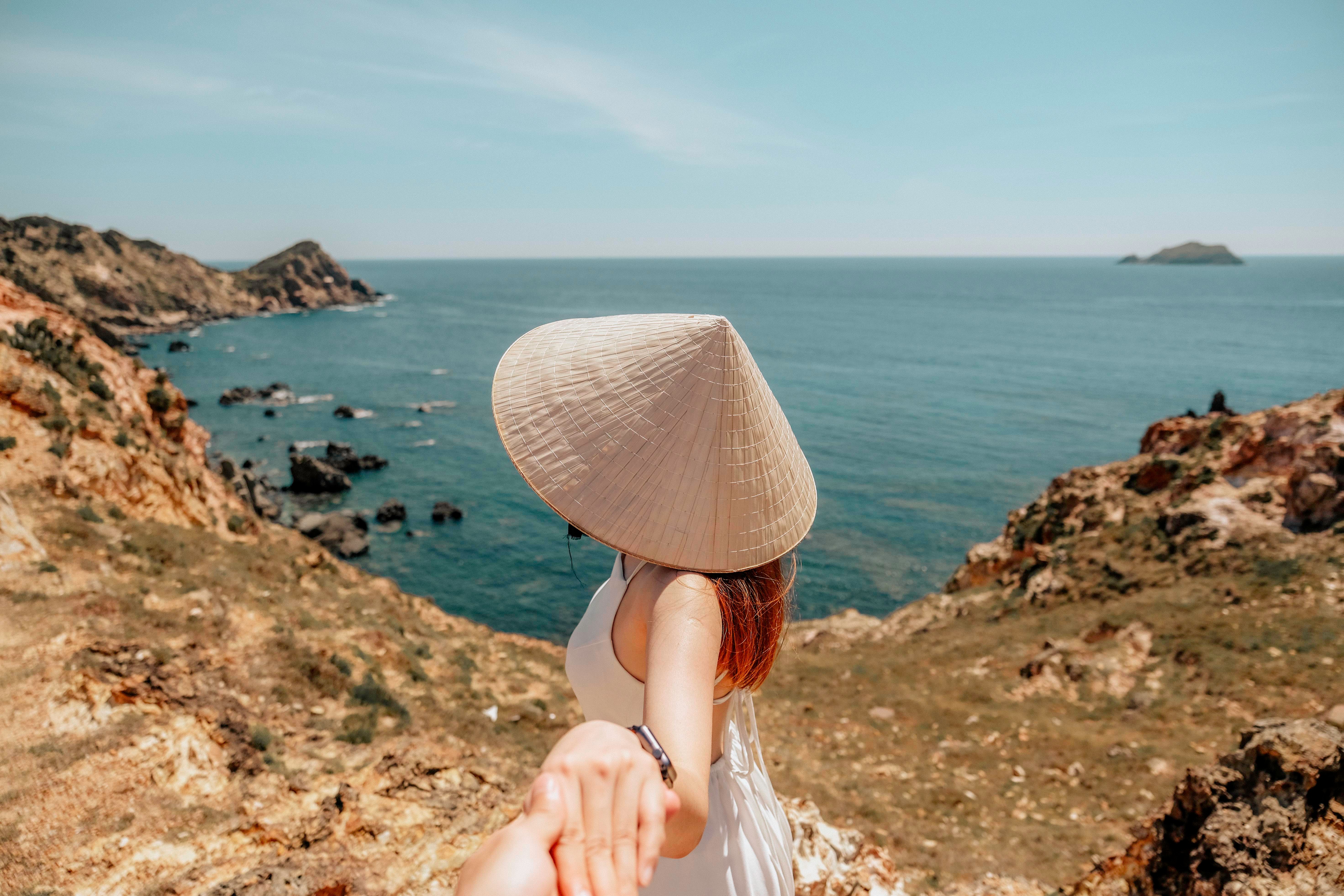 A woman in traditional hat holds hands, overlooking the stunning coastline of Quy Nhơn, Vietnam.