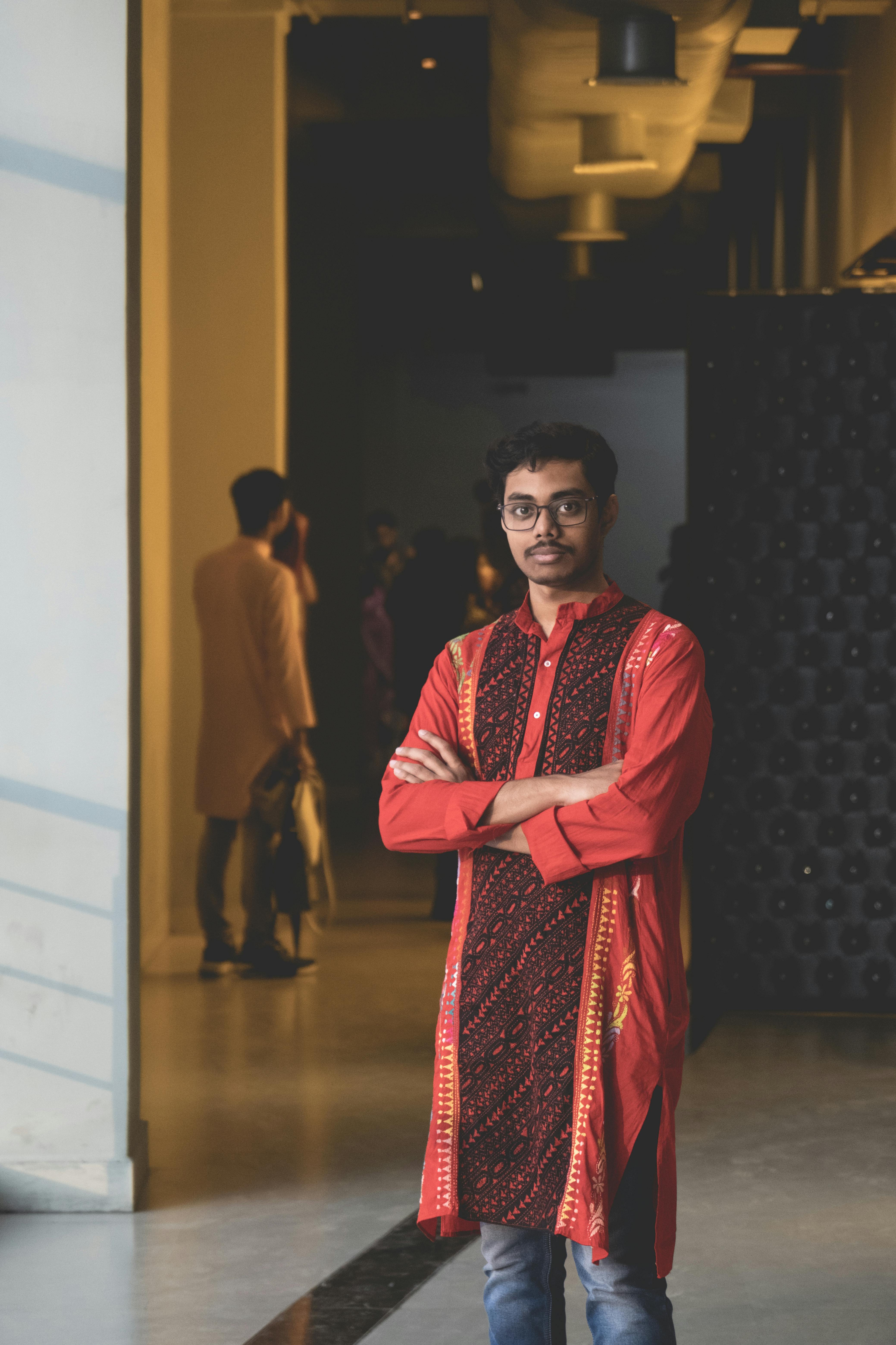 Man in traditional clothing poses indoors, showcasing cultural fashion style.