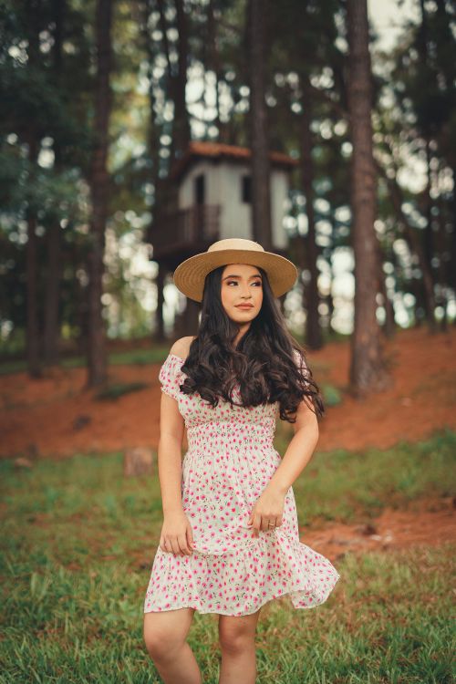 Free A young woman with long hair in a floral dress stands in a forest wearing a sun hat. Stock Photo