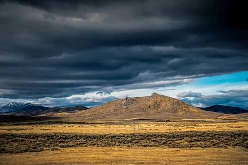 Free A stunning view of dark storm clouds looming over a desolate arid mountain landscape, creating a moody atmosphere. Stock Photo