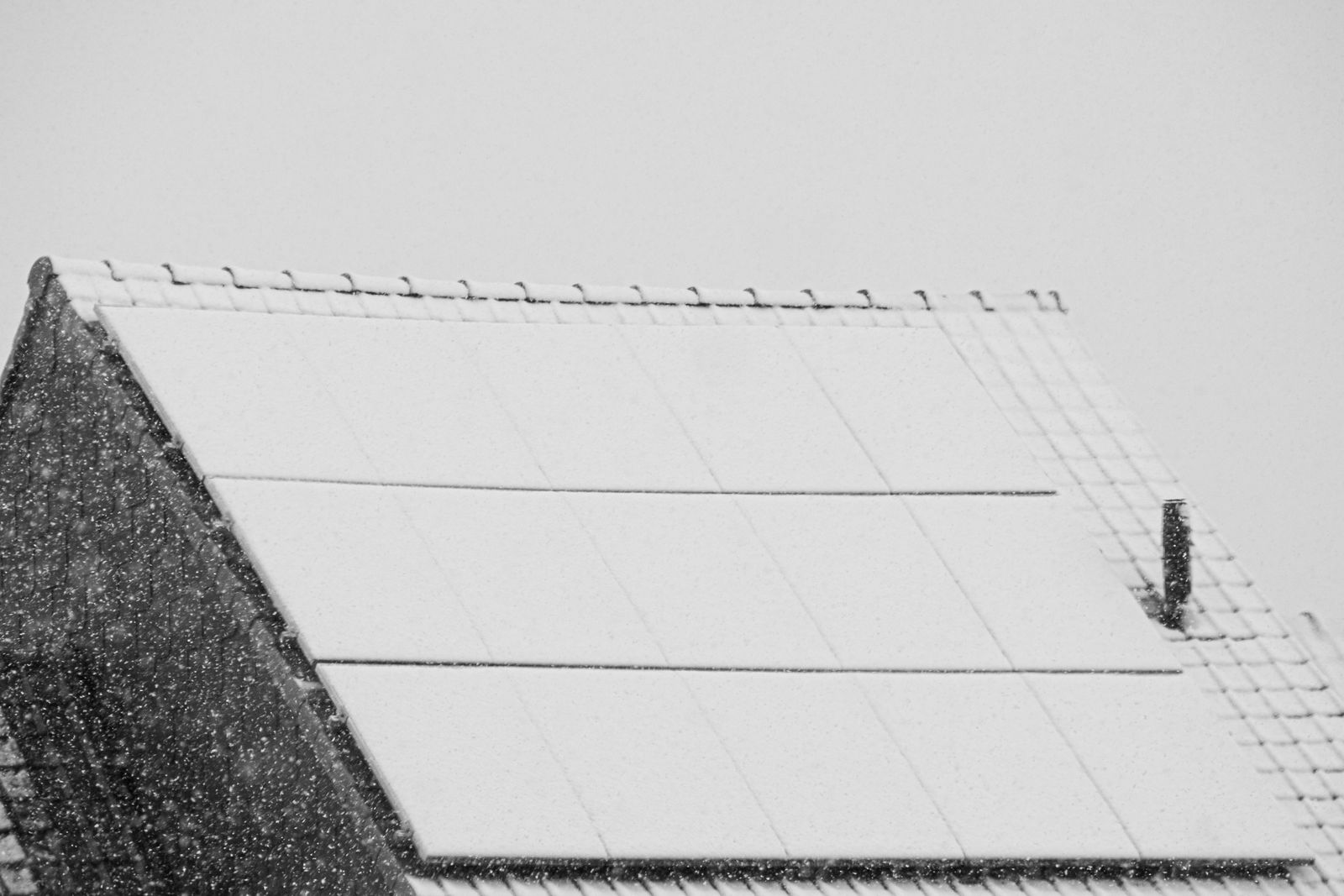 Schneebedeckte Solarmodule auf einem Ziegeldach bei Schneefall