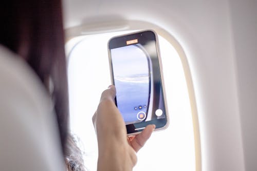 Close-up of a Woman Recording a Video of the View from an Airplane Window
