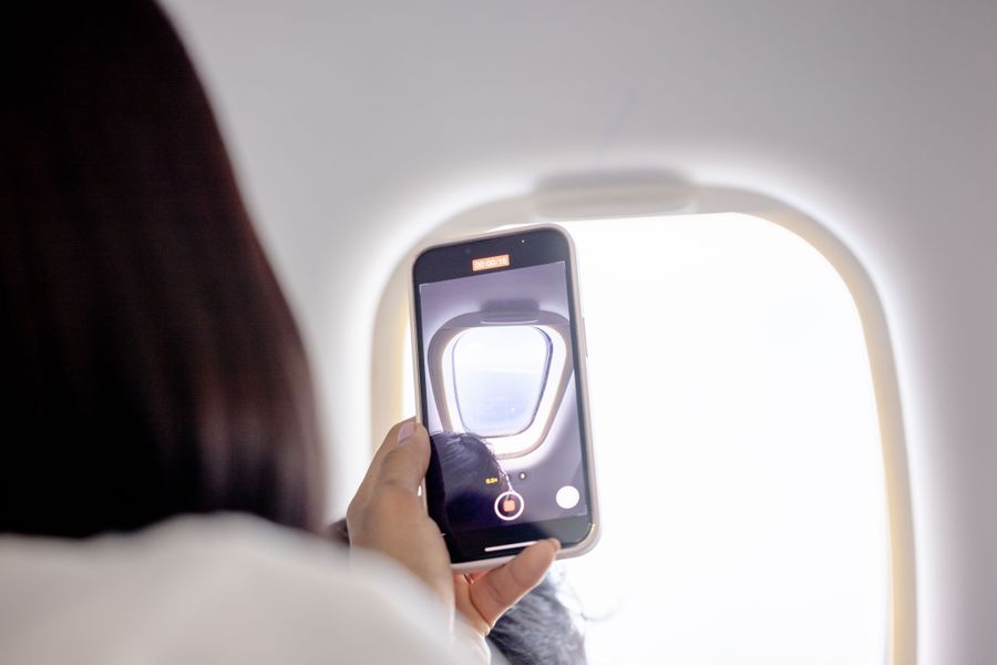 A passenger holding a smartphone up to the window inside an airplane