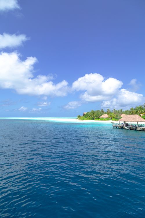 Free Serene tropical beach scene with overwater bungalows under a bright blue sky and clear ocean waters. Stock Photo