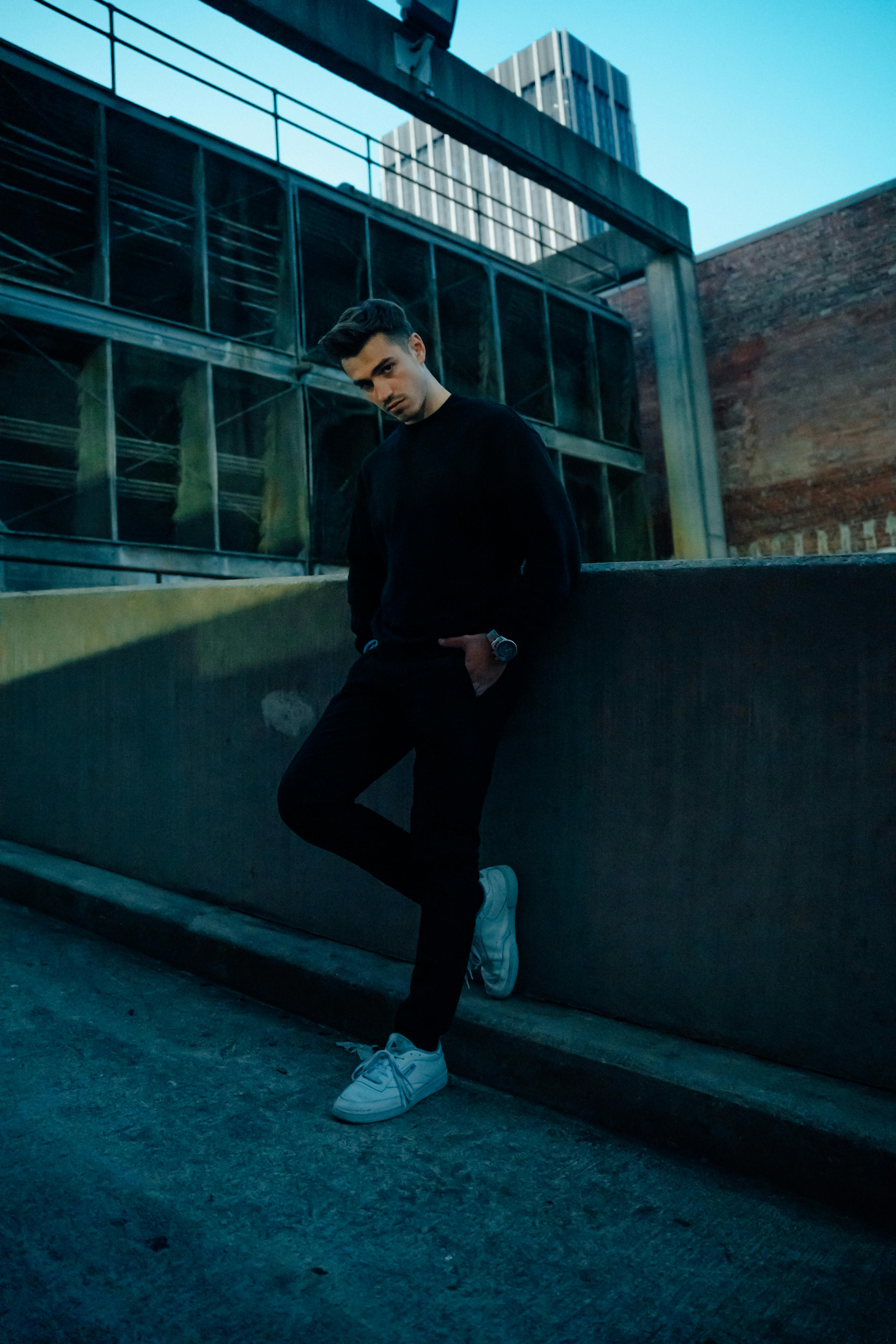 Moody urban portrait of a stylish man leaning against a city wall.