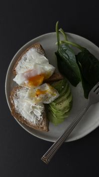 Delicious avocado toast topped with a fried egg and fresh spinach on a plate.