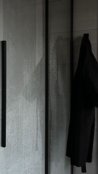 Black jacket hanging in a minimalist bathroom with glass shower door.