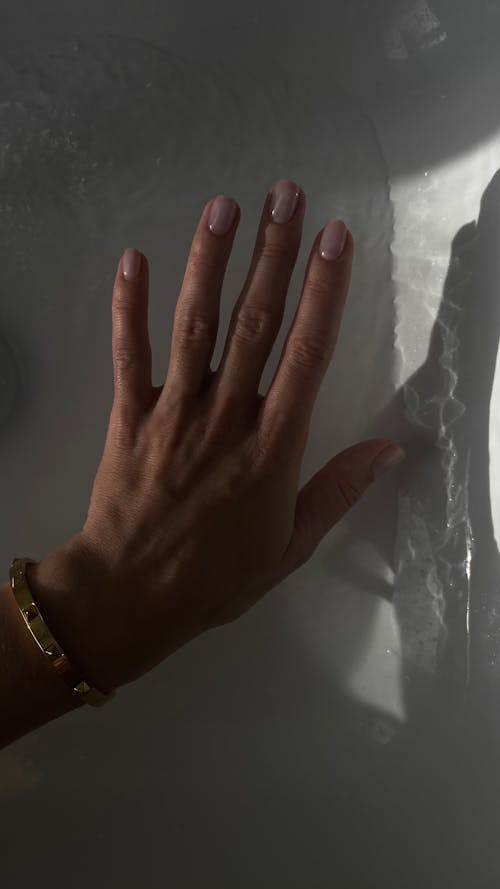 A Hand of a Woman with Painted Nails on the Background of a White Wall 