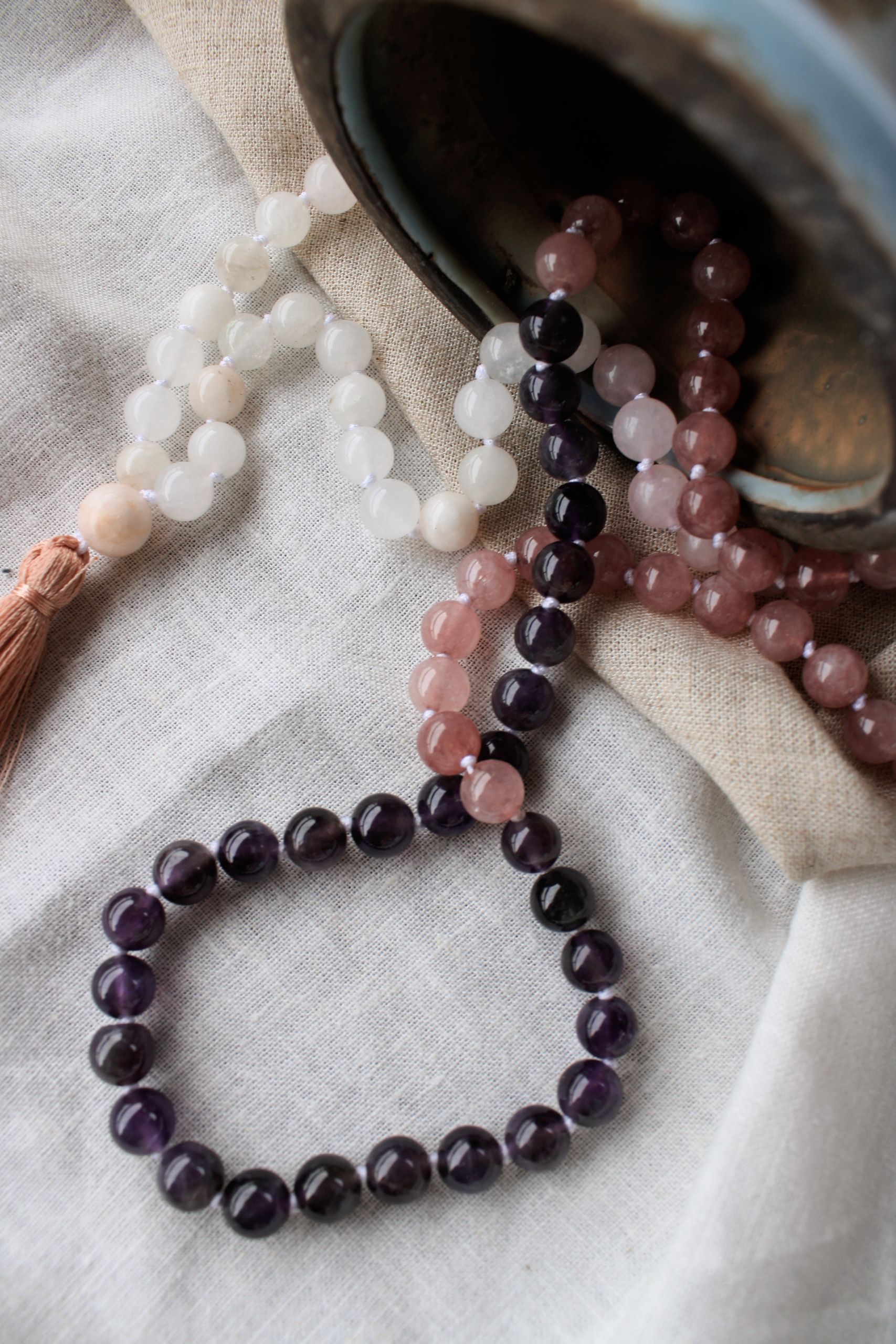 Prayer beads spill from a pot onto linen, symbolizing spirituality and meditation.