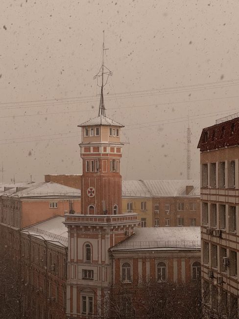 Snow gently falls over a historic urban building, creating a serene winter scene.