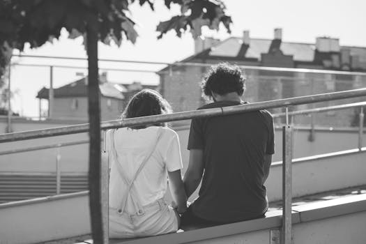 Grayscale Photo of Man and Woman Sitting on Inclined Road