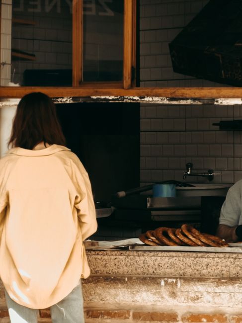 Woman buying fresh pastries from a street bakery window in an urban setting.