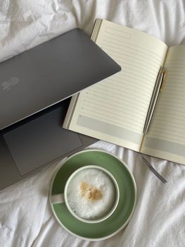 A cozy home office setting with a laptop, notebook, and coffee on a bed, perfect for remote work.