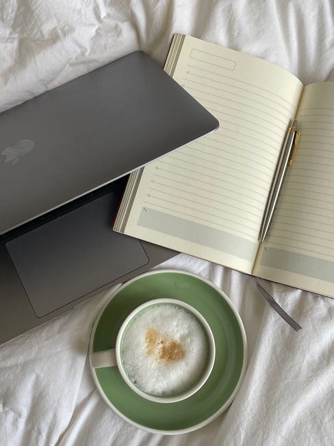 A cozy home office setting with a laptop, notebook, and coffee on a bed, perfect for remote work.