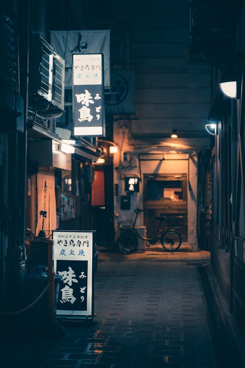 A Narrow Alley between Buildings and Neon Signs in City at Night 