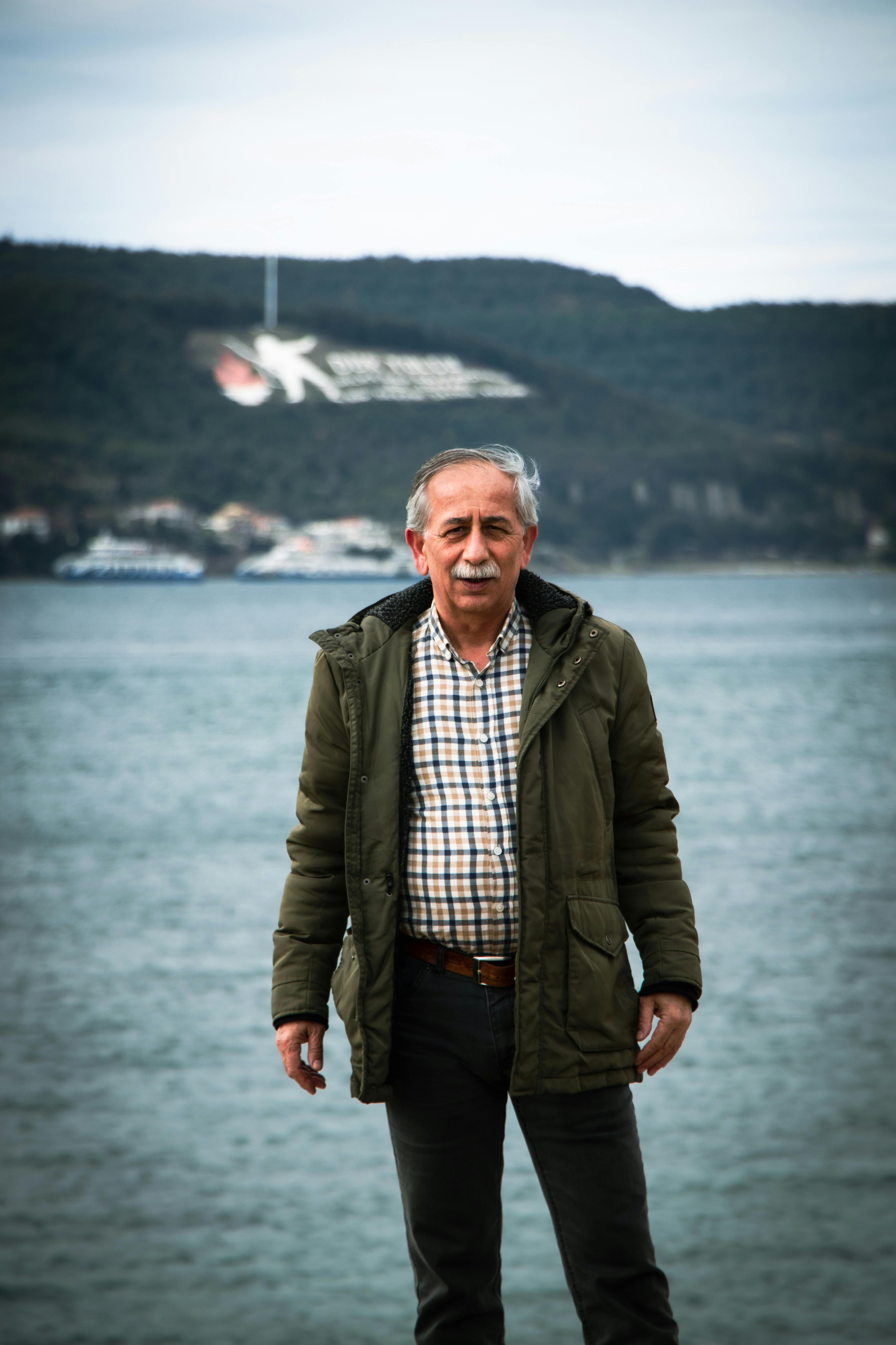 Elderly man standing by the sea with hills in the background on a winter day.