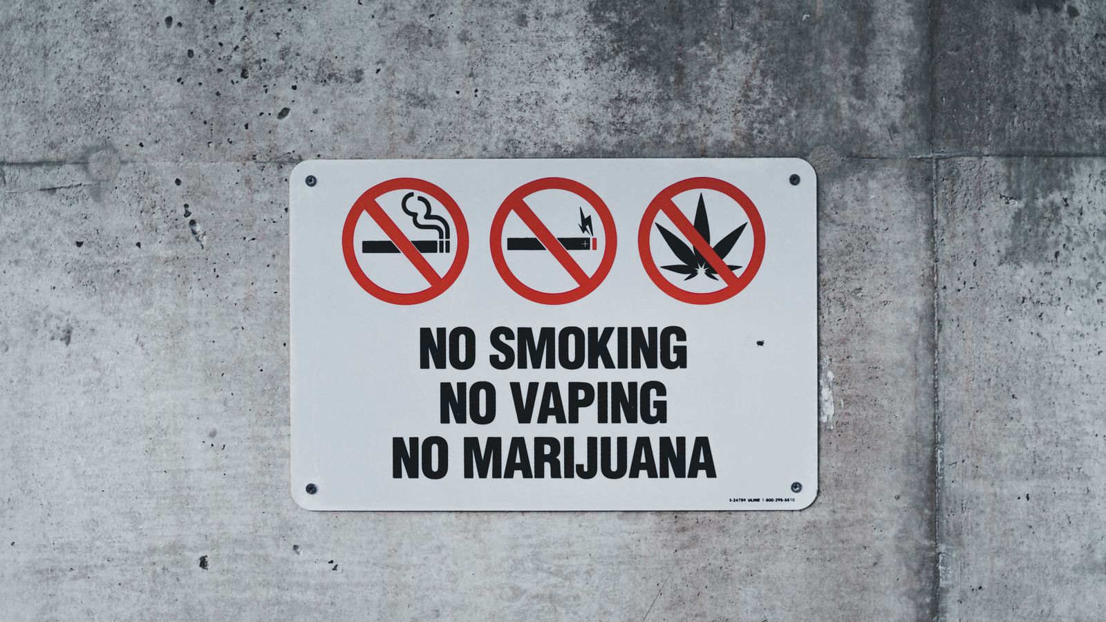 A clear warning sign prohibiting smoking, vaping, and marijuana on a concrete wall.