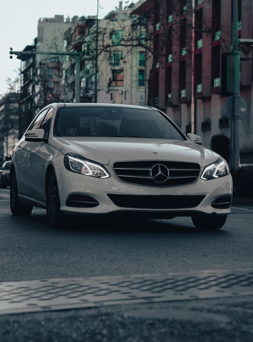 Free A white luxury car driving on a city street in İzmir, Türkiye, showcasing urban life. Stock Photo