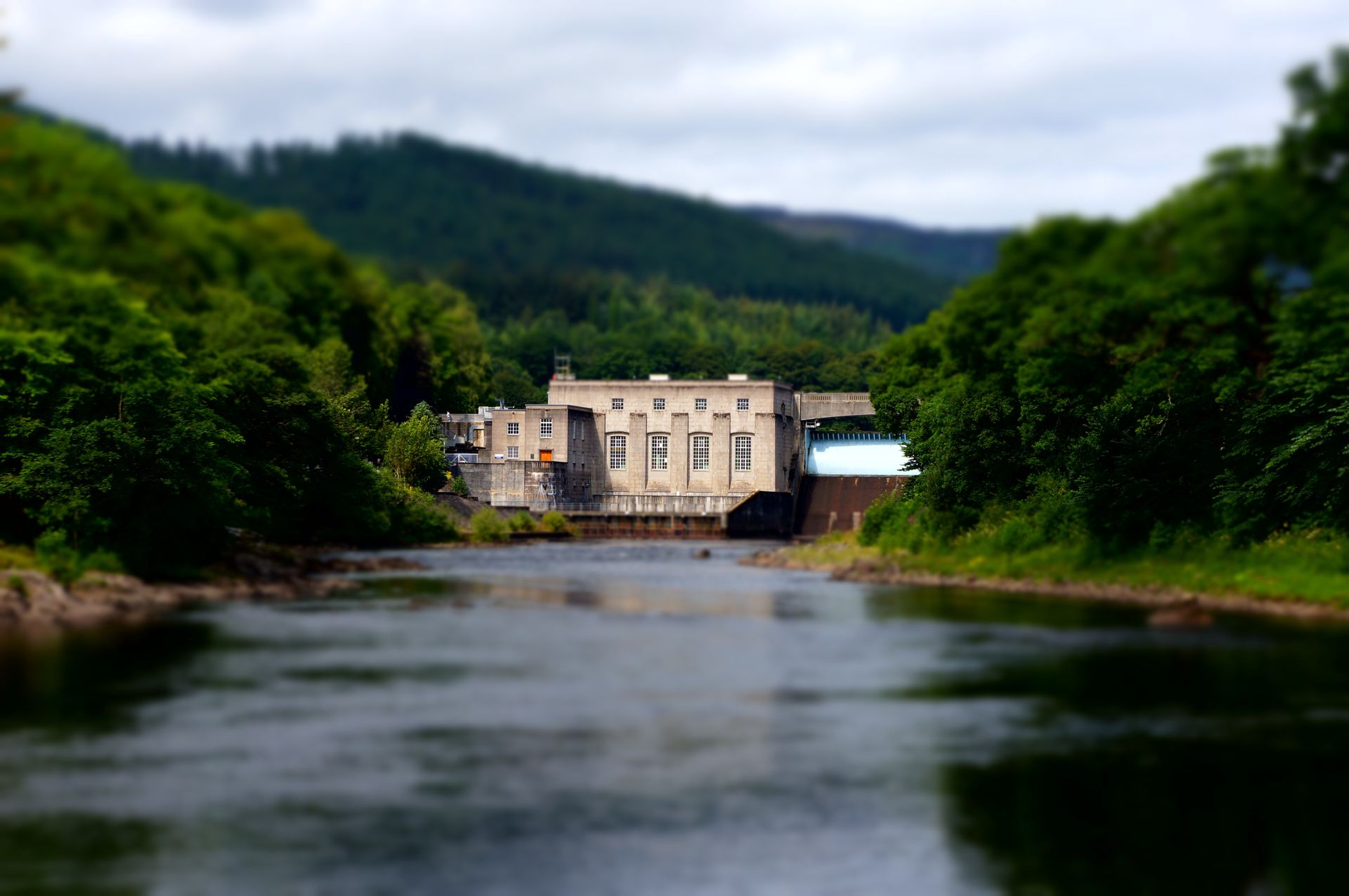 Scenic view of a hydroelectric power station on a river surrounded by lush forest.