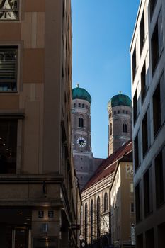 Munich's Frauenkirche towers framed by city buildings under a clear sky.