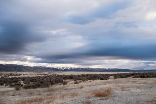 Free Expansive desert landscape with dramatic clouds and distant mountains in twilight. Stock Photo