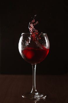 Dynamic shot of red wine splashing in a glass against a dark backdrop, creating a vibrant and elegant effect.