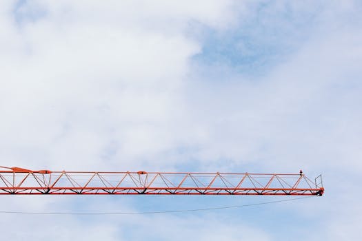 红色工业起重机臂在明亮的蓝天下伸展，云朵蓬松