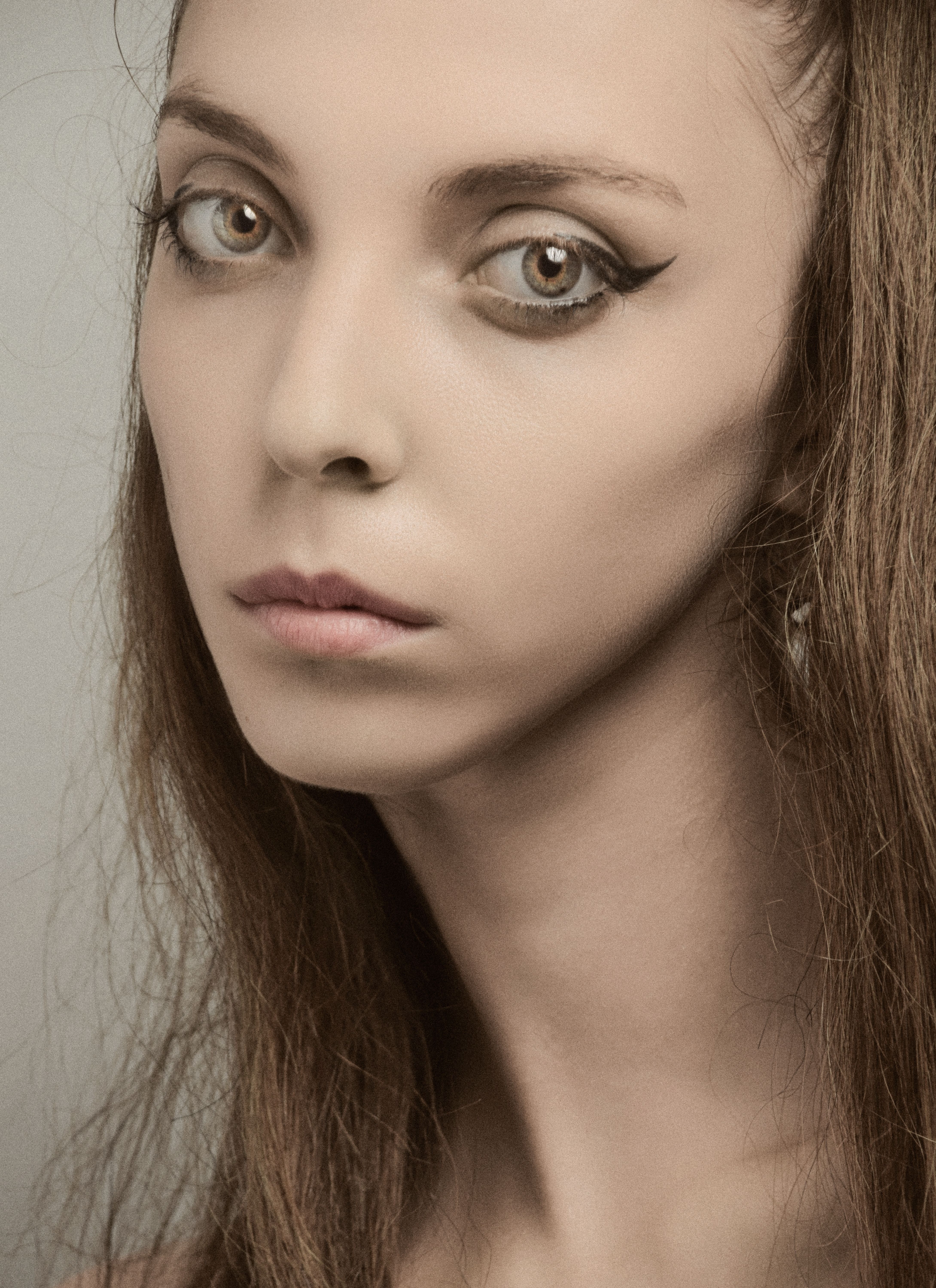 Close-up studio portrait of a woman with striking eyes and subtle makeup, set against a neutral background.