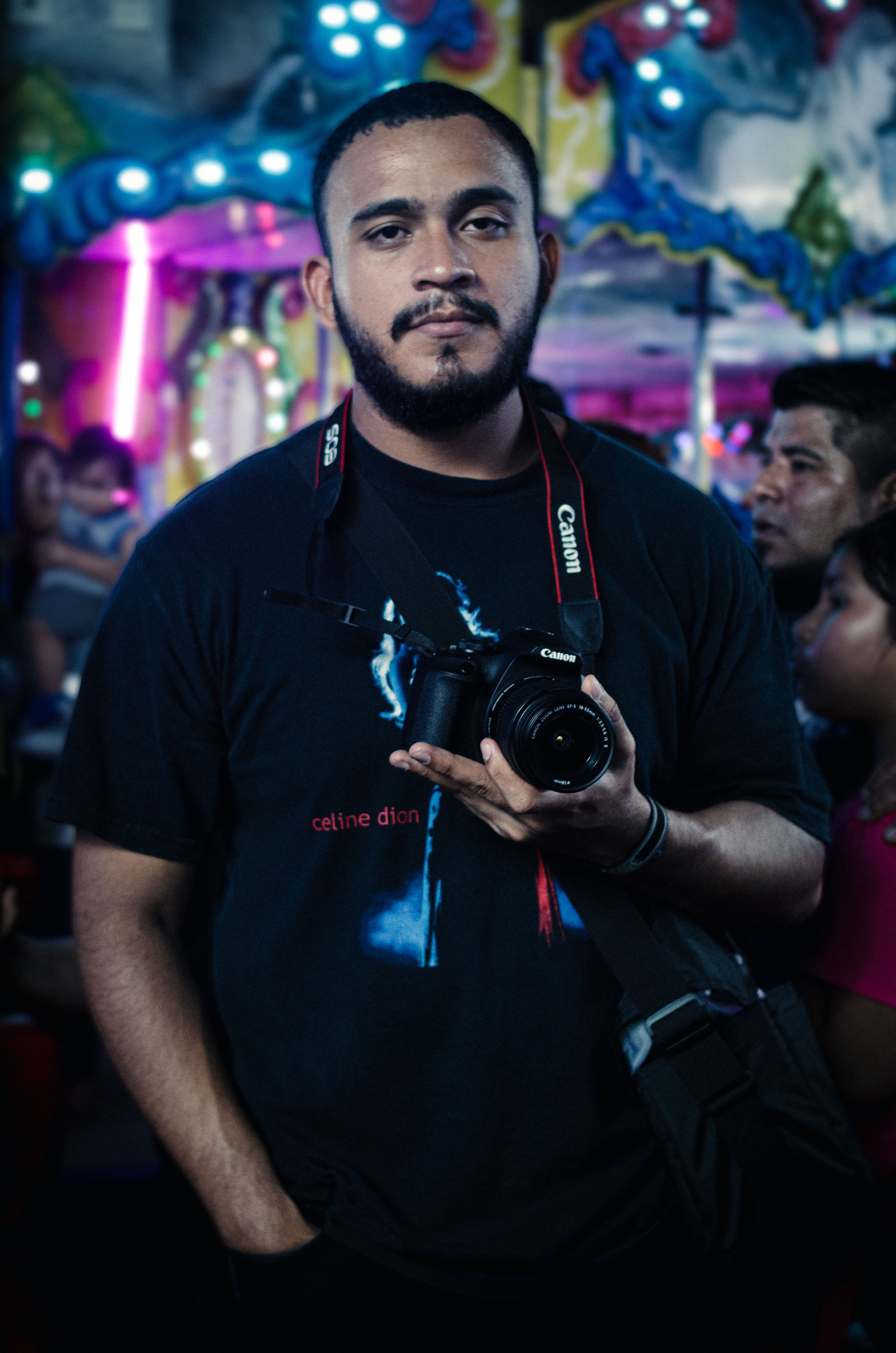 A portrait of a man holding a camera at a lively night funfair setting.