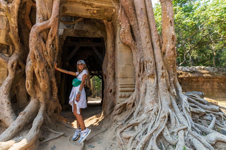 Woman Standing Next To Huge Roots Of A Tree On A Temple Ta Som Gate In Angkor Wat Complex At Siem Reap, Cambodia