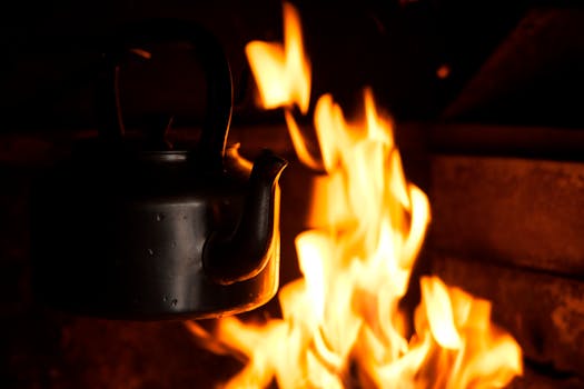 A black kettle suspended over bright flames, showcasing warmth and intensity.