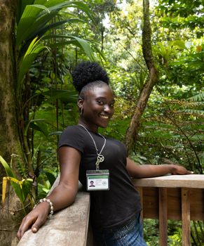 Photo by Sean P. Twomey Young woman with ID badge smiling on a terrace in a tropical forest setting.