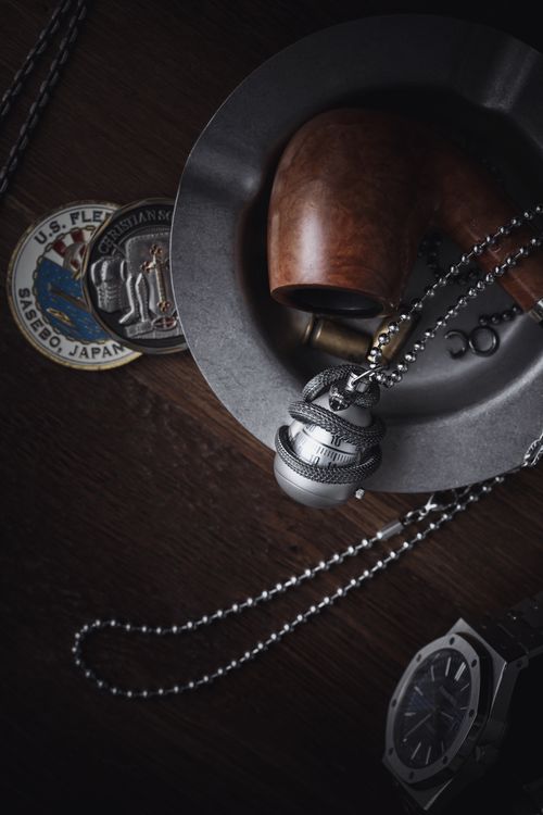 Free A stylish arrangement featuring silver jewelry, a wooden pipe, and nautical badges, captured in a moody environment. Stock Photo