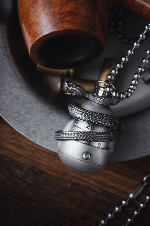 Free Close-up of a silver necklace featuring a snake design, placed on textured wood, exuding elegance and mystery. Stock Photo