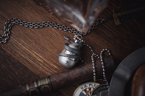 Free Silver snake pendant on a chain with cigar on wooden surface. Elegant top view shot. Stock Photo