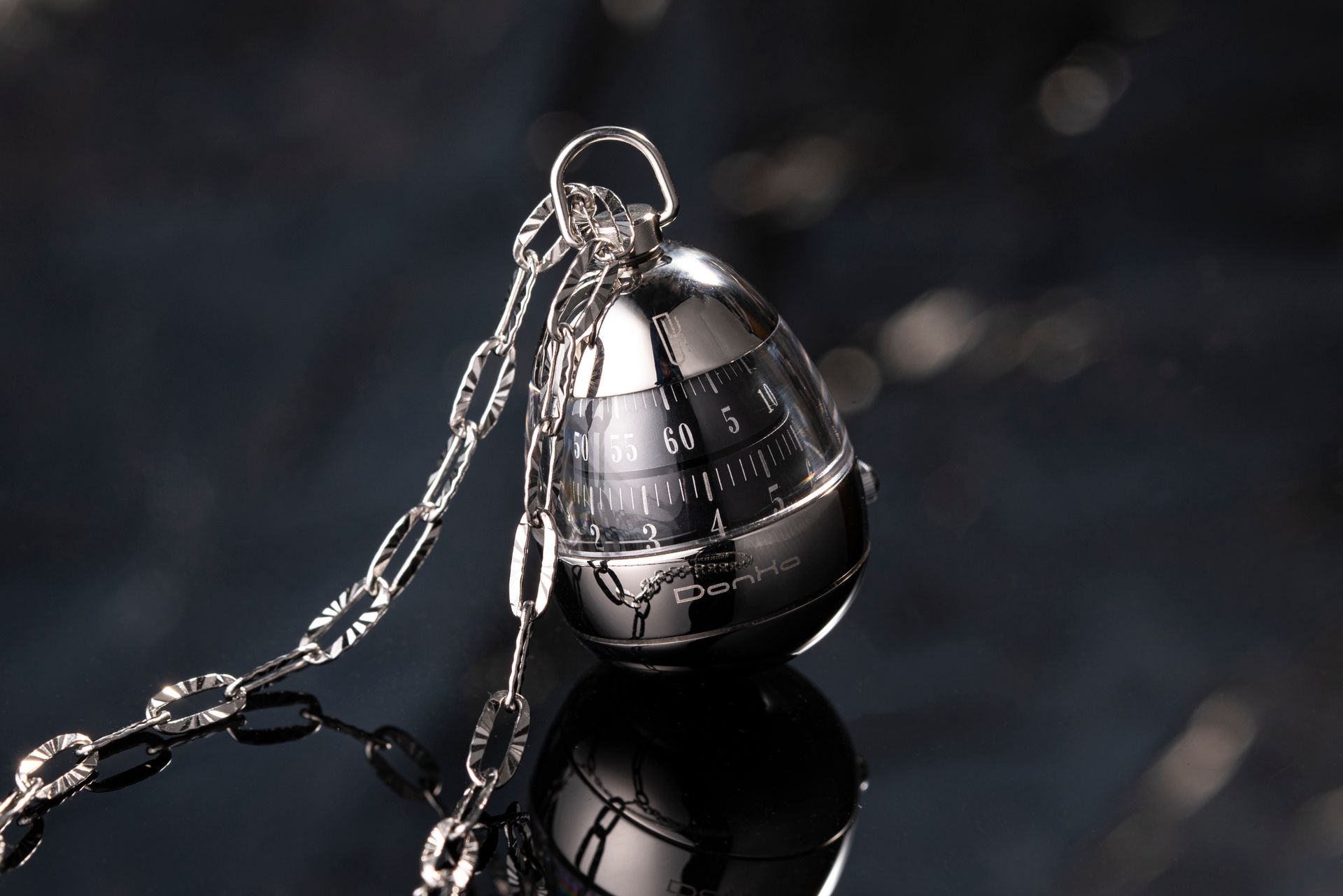Silver egg-shaped kitchen timer with chain on a reflective surface, showcasing elegant design.