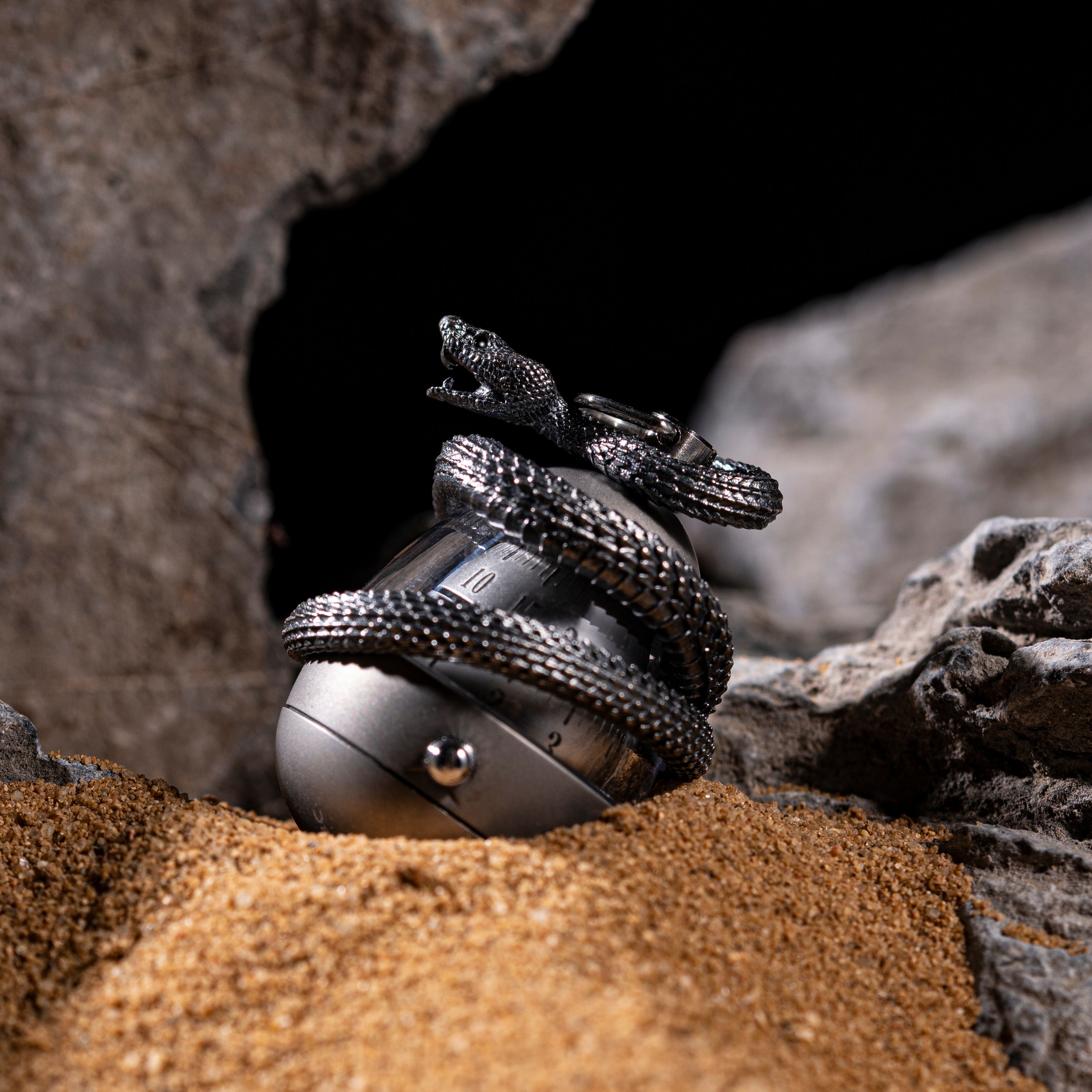 Artistic display of silver snake jewelry amidst sand and rocks, highlighting intricate details.
