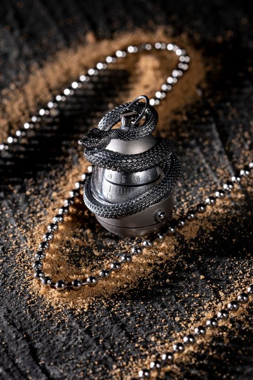 Free A stunning silver pendant shaped like a snake egg with chain, artistically captured on dark sand. Stock Photo
