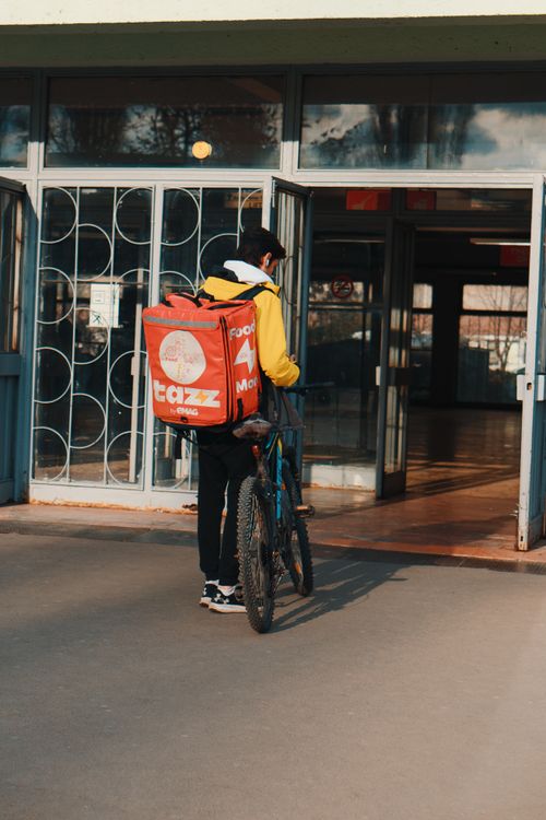 Free Delivery cyclist with a large red bag entering a building through an open doorway. Stock Photo
