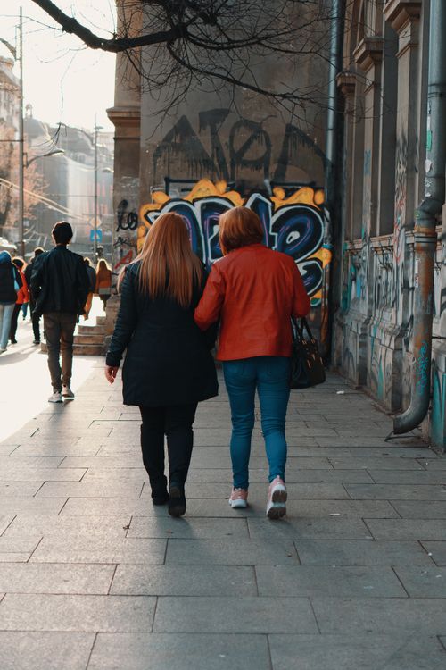 Free Two women walking past graffiti-covered walls on a sunny city street. Stock Photo
